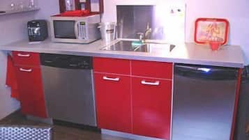 A compact kitchen with a microwave, coffee maker, and a red toaster on the countertop.