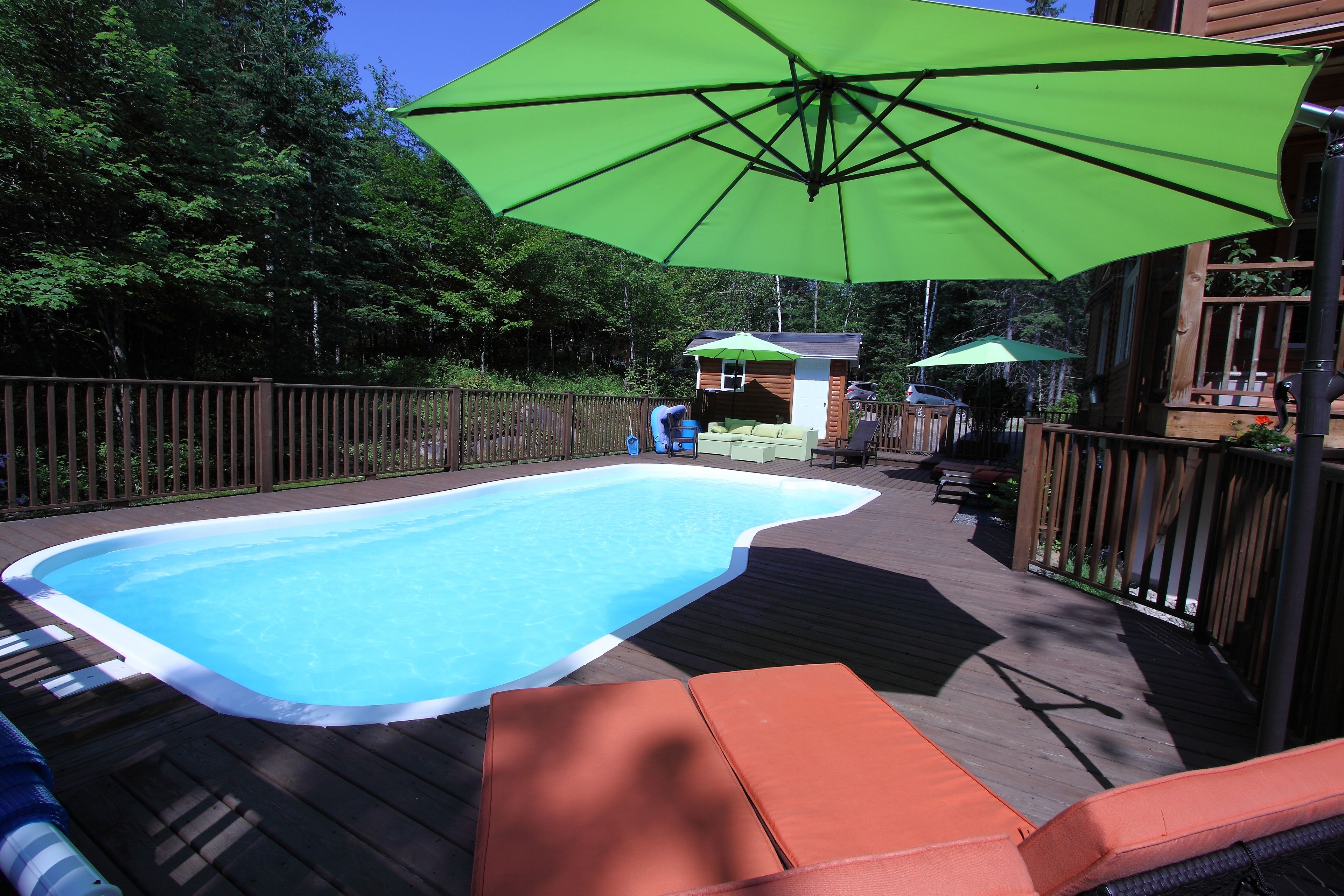 A swimming pool with a wooden deck, lounge chairs, and a green umbrella.
