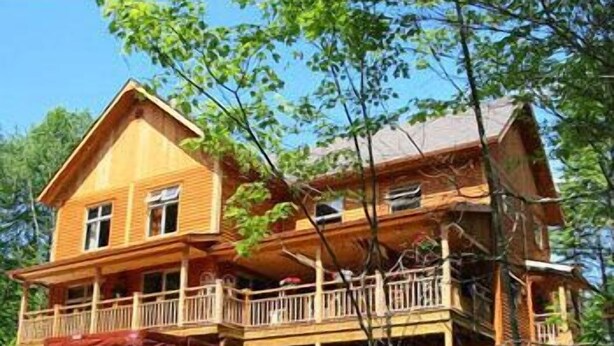 A two-story wooden cabin with a balcony, surrounded by trees and a rocky landscape. - Escale du Nord (Mont-Tremblant)