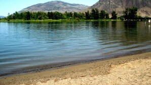 Un lago tranquilo con orilla arenosa y una montaña al fondo.