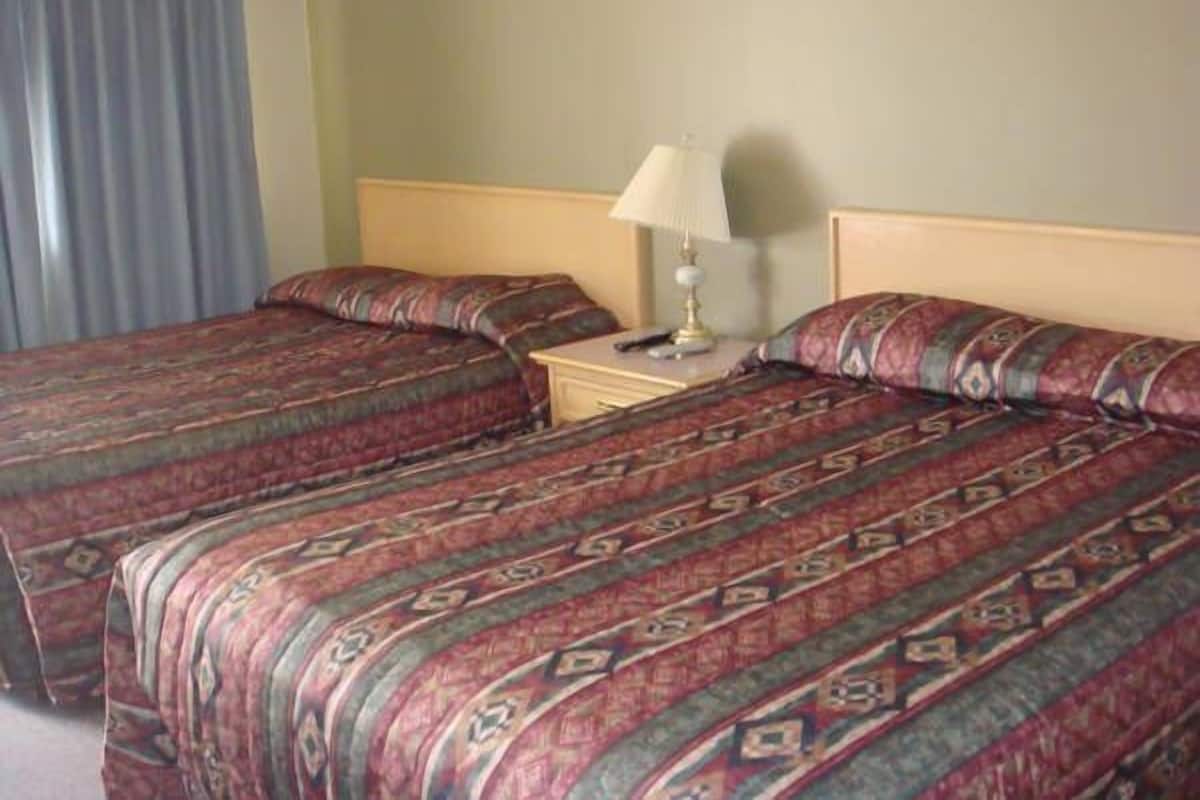 A hotel room with two beds, a nightstand with a lamp, and a window with curtains.