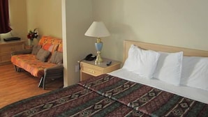 Habitación de hotel con cama, mesita de noche con lámpara, una silla y una pequeña mesa con un jarrón de flores.
