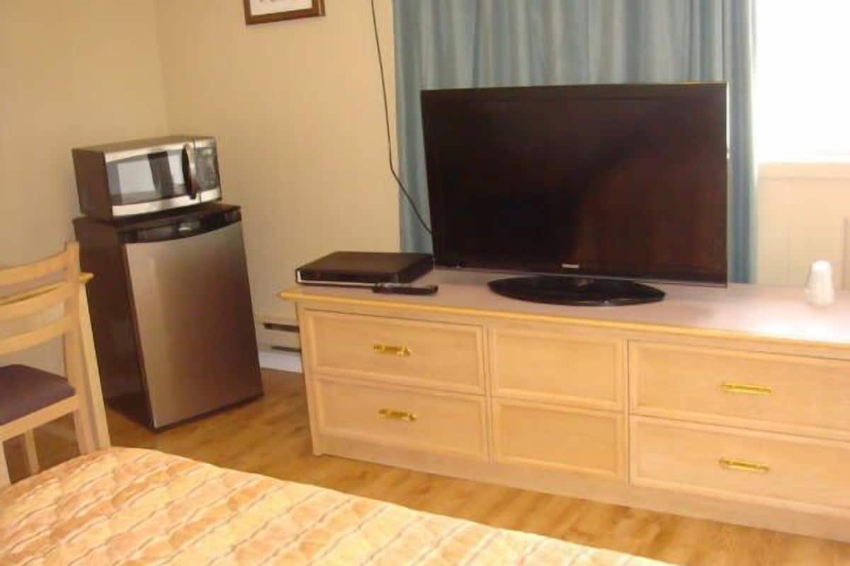 A hotel room with a bed, a desk with a television, a microwave, and a chair.