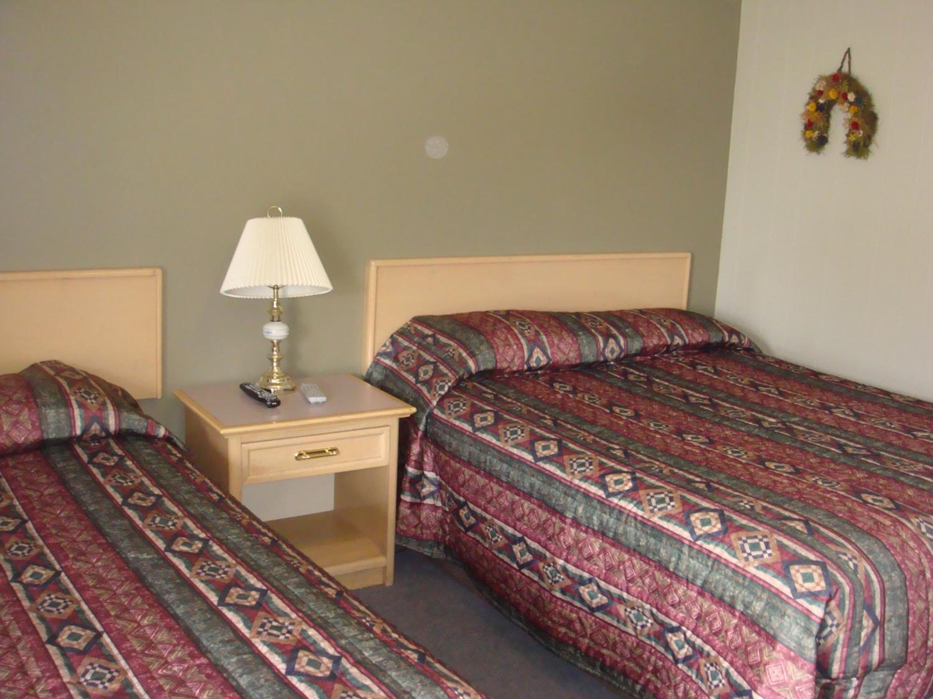 A bedroom with two beds, a nightstand, a lamp, and a remote control.