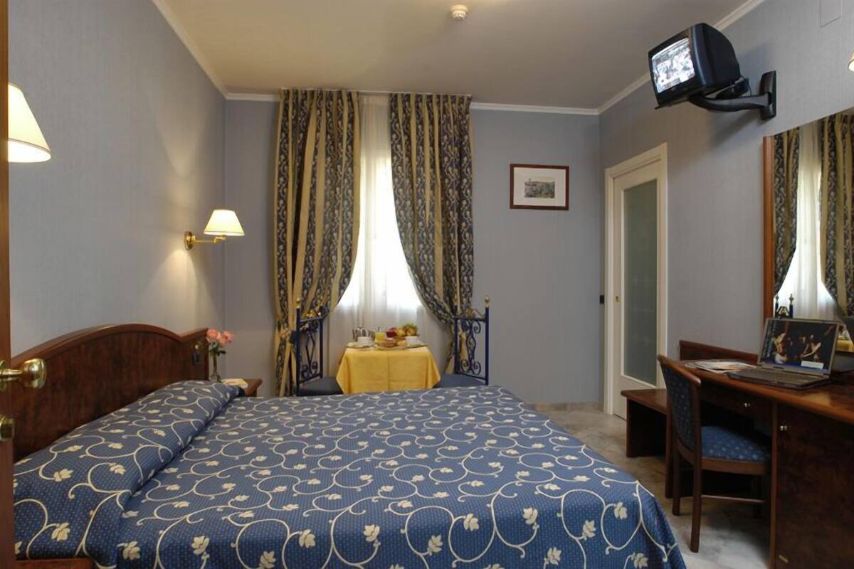 A hotel room with a bed, a desk with a chair, a television, and curtains.