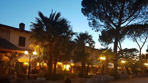 Un patio con mesas al aire libre, palmeras y un muro de piedra.