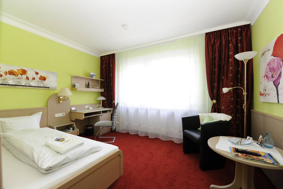 Ein Hotelzimmer mit Bett, Schreibtisch, Stuhl und einem kleinen Tisch mit Lampe.