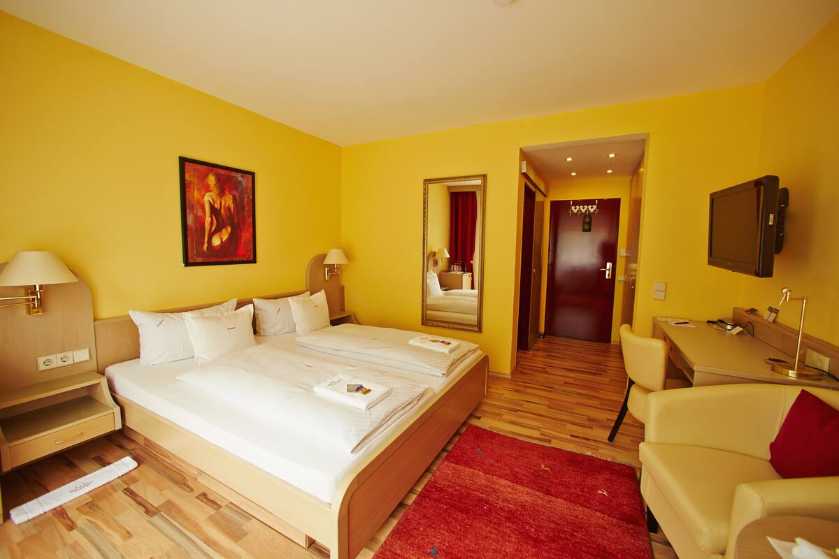 Ein Hotelzimmer mit einem großen Bett, einem Schreibtisch, einem Sessel und einem Fernseher.