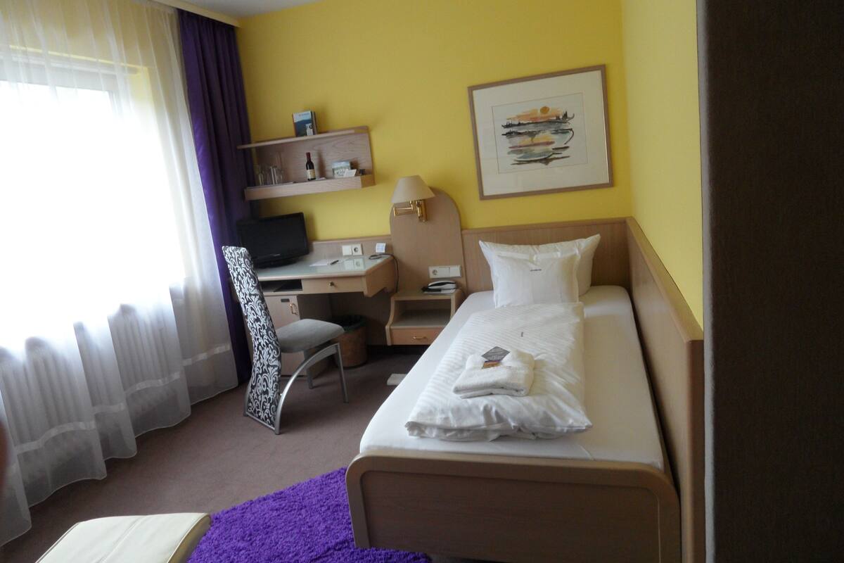 Ein Hotelzimmer mit Bett, Schreibtisch, Stuhl, Fernseher und einem Fenster mit Vorhängen.