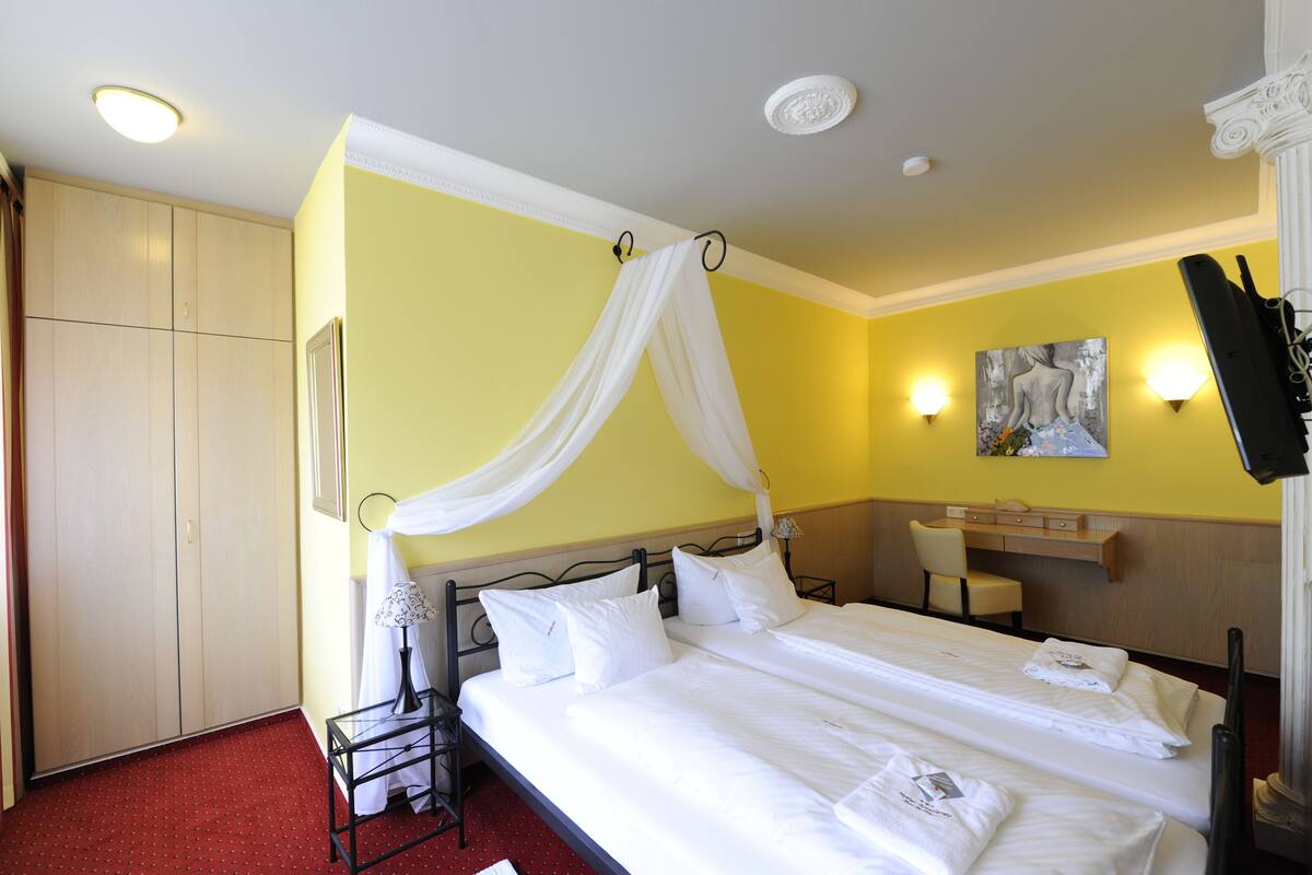 Ein Hotelzimmer mit Bett, Nachttisch, Sessel, Kleiderschrank und einem Gemälde an der Wand.