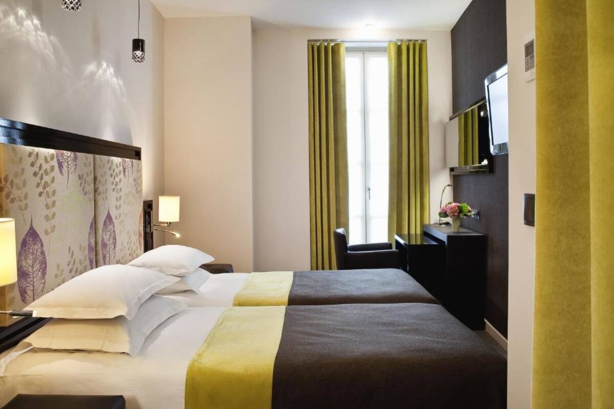 Ein Hotelzimmer mit zwei Betten, einem Schreibtisch, einem Sessel, einem Fernseher und einem Fenster mit Vorhängen.