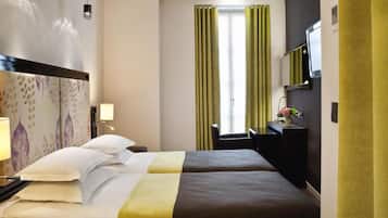 Een hotelkamer met twee bedden, een bureau, een stoel, een televisie en een raam met gordijnen.