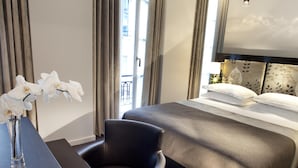 A hotel room with a bed, a desk with a vase of flowers, a chair, and a large window with curtains.