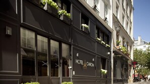 A building with a sign reading "HOTEL CARON PARIS" and balconies with plants.
