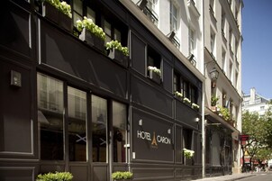A building with a sign reading "HOTEL CARON PARIS" and balconies with plants.