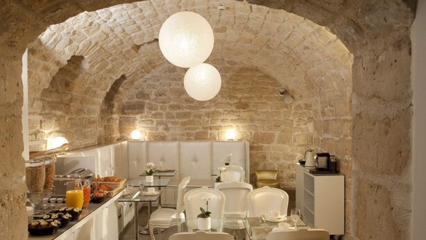 A stone-walled dining area with white chairs and tables, a buffet with breakfast items, and a coffee machine.
