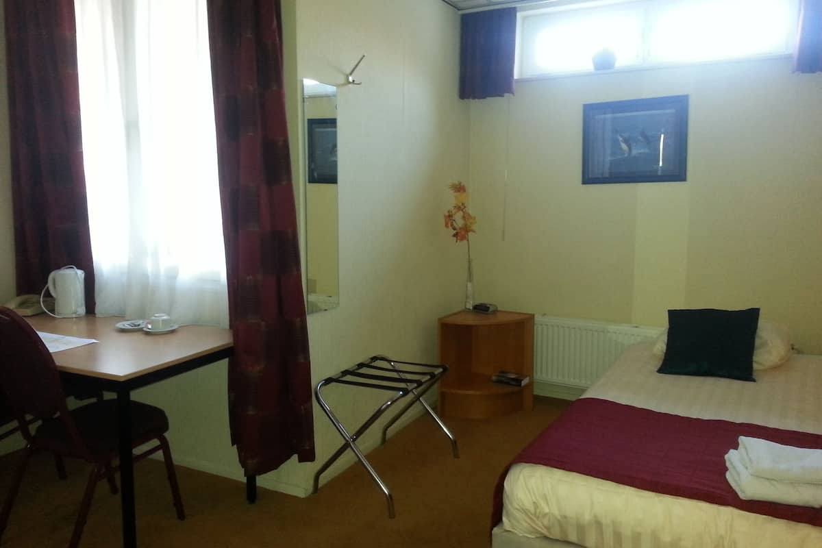 Une chambre d’hôtel avec un lit, un bureau, une chaise, un radiateur et une fenêtre avec des rideaux.
