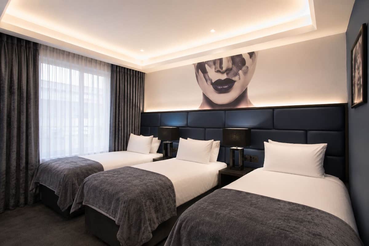 A hotel room with two beds, a large wall art piece, and a modern ceiling design.