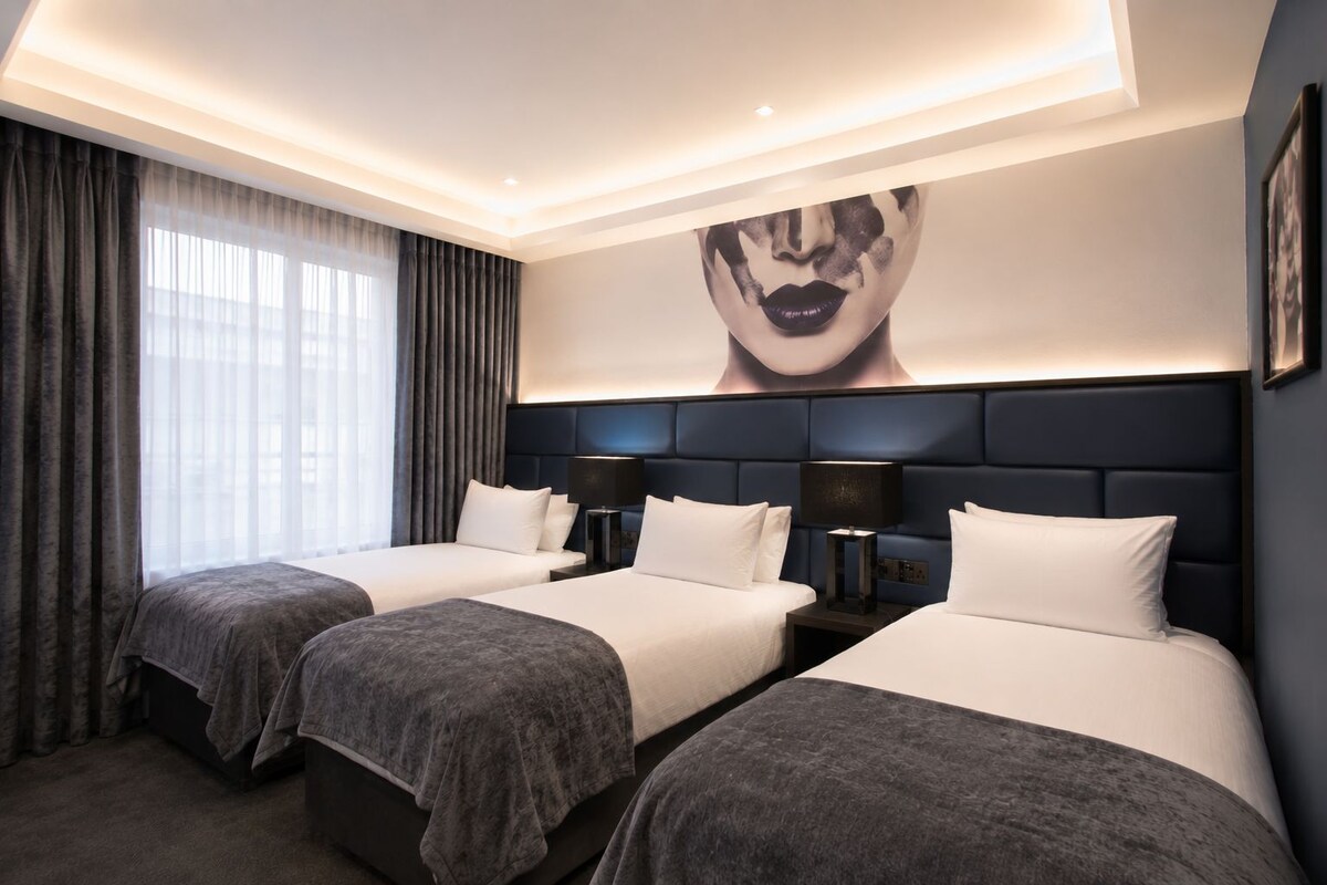 Habitación de hotel con dos camas, una obra de arte grande en la pared y un diseño moderno en el techo.
