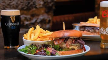 Plat amb una hamburguesa, patates fregides i amanida, acompanyat de dues begudes, una de les quals és una cervesa Guinness.
