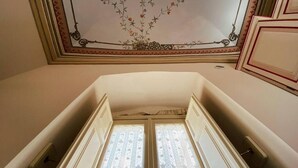 A room with a high ceiling, a decorative ceiling design, and a window with a patterned curtain. - Hotel Palazzo Gambuzza - Ispica (Ispica)
