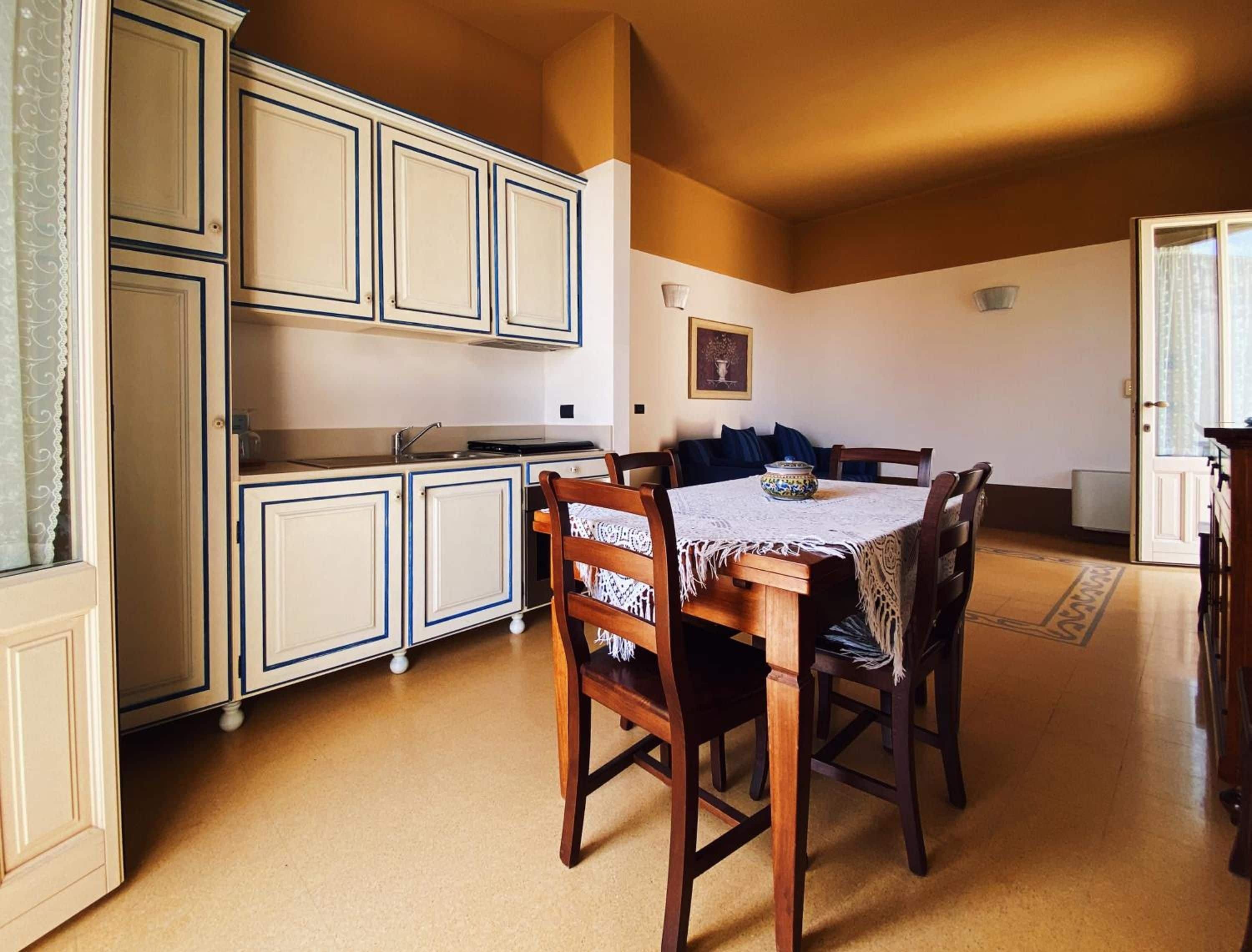 Un comedor con mesa y sillas, una cocina con armarios, y una puerta que da a otra habitación.