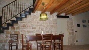 A dining area with a stone wall, wooden staircase, and a table with chairs. - Hotel Palazzo Gambuzza - Ispica (Ispica)