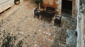 A building with a tiled roof, a stone archway, and a small patio area with a bench and potted plants. - Hotel Palazzo Gambuzza - Ispica (Ispica)