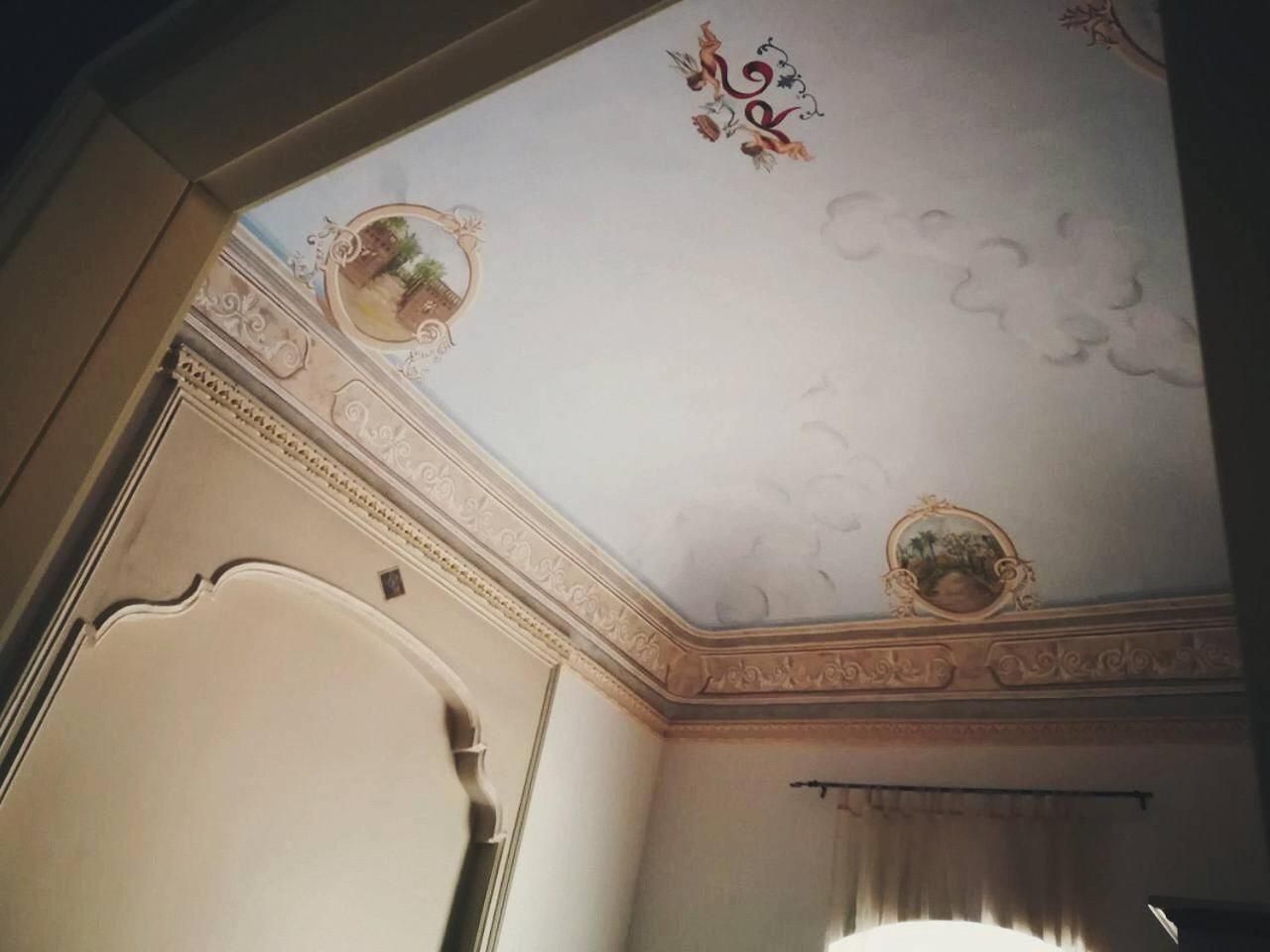 Una habitación con un techo decorativo, molduras ornamentales y un cuadro enmarcado.