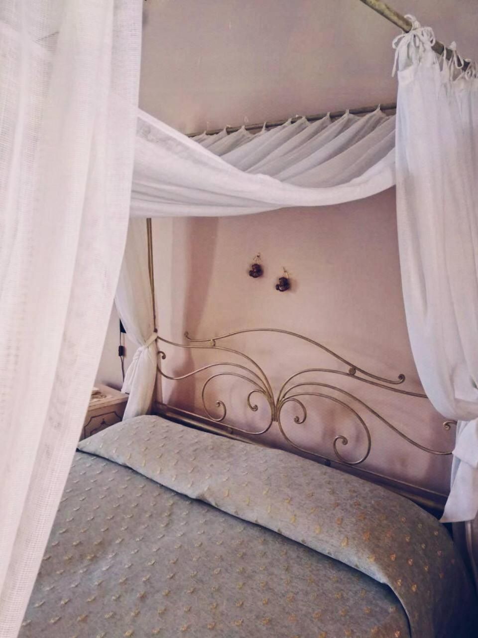 A bed with a metal headboard, white curtains, and a patterned bedspread.