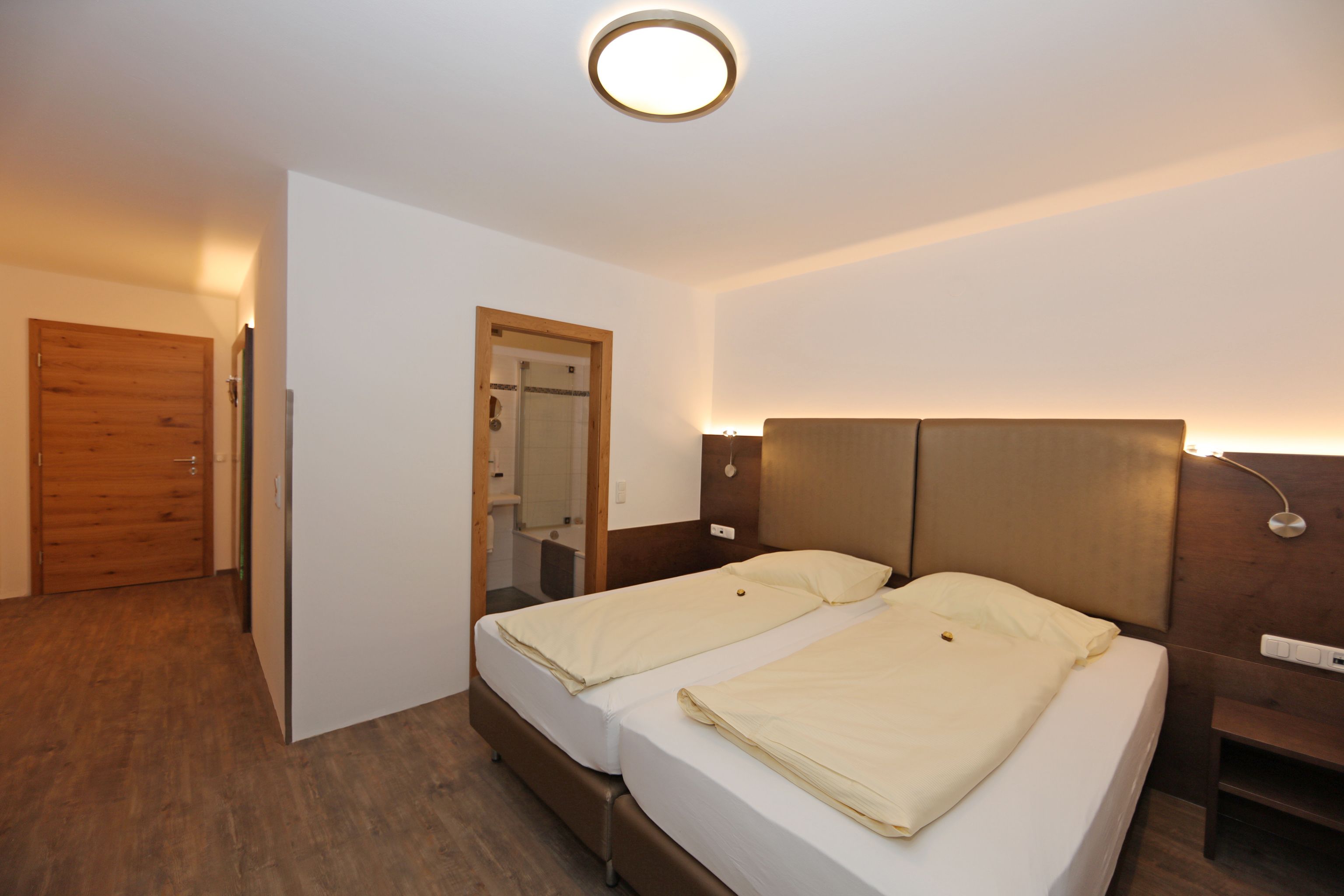 A hotel room with two beds, a wooden door, a mirror, and a bedside table.