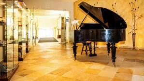 Un piano de cola en un amplio vestíbulo con piso a cuadros y vitrinas de vidrio.