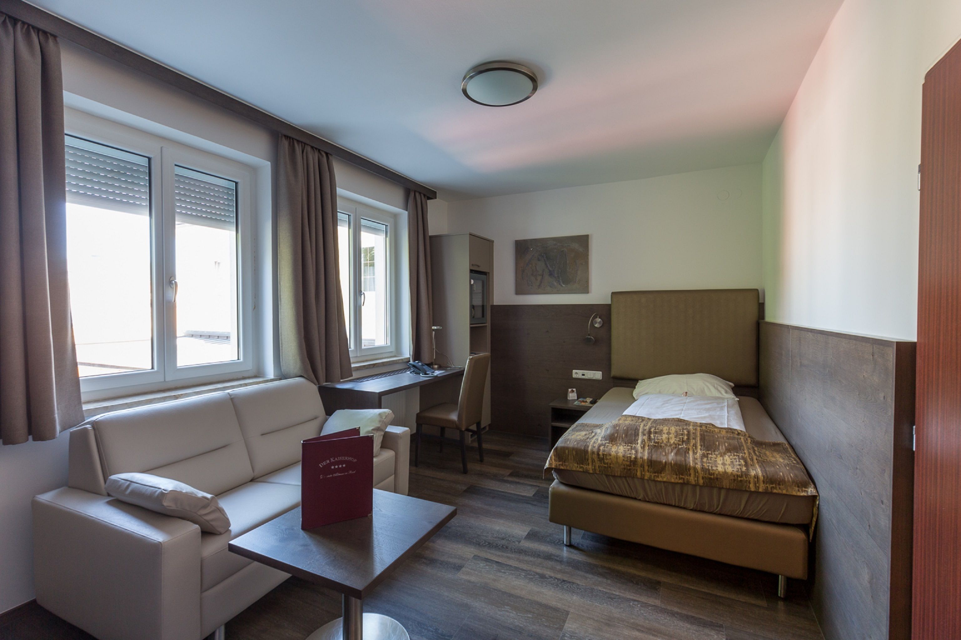 A hotel room with a bed, a desk, a chair, a sofa, and a window with curtains.