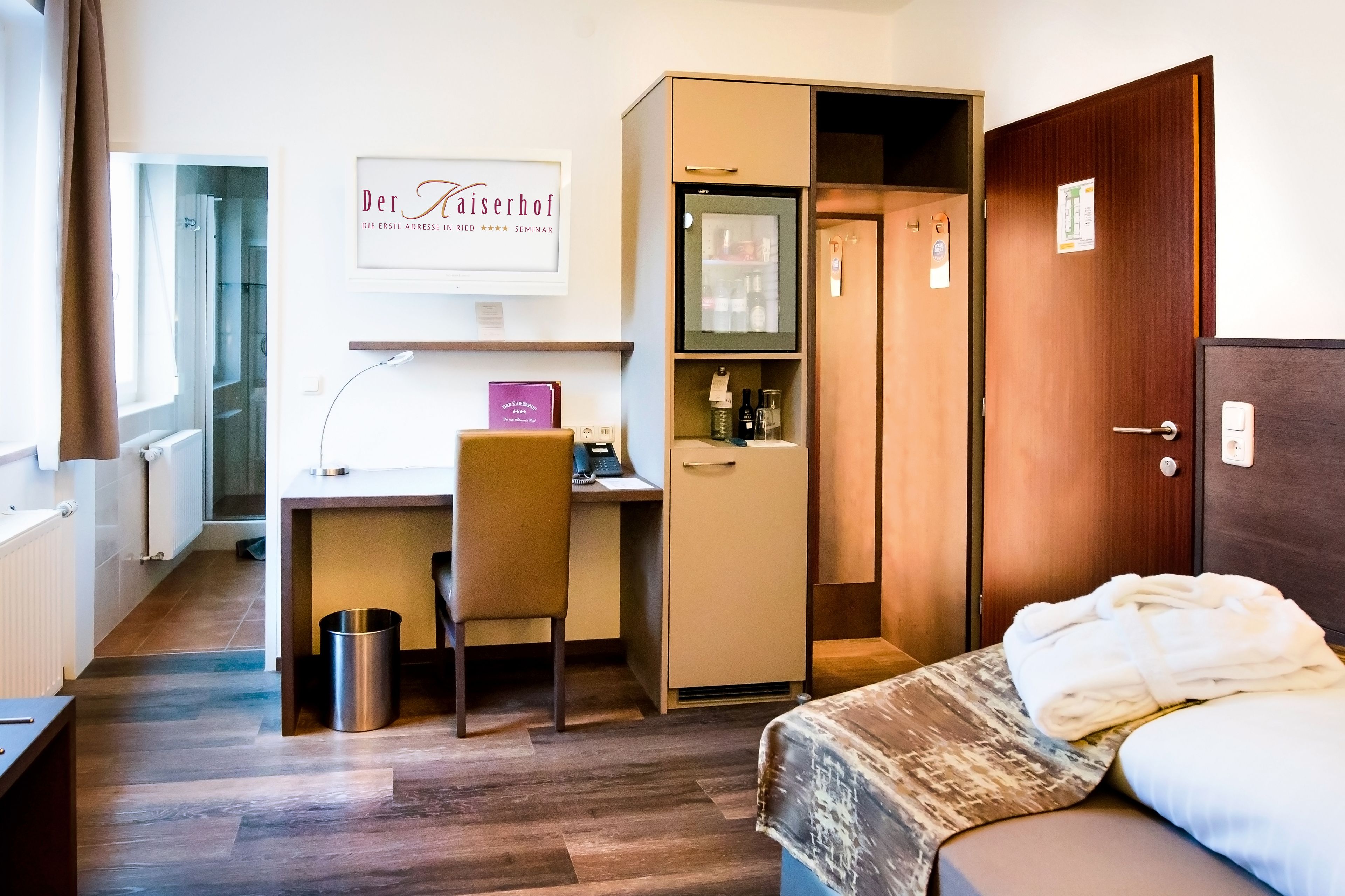 Habitación de hotel con cama, escritorio, silla, armario y zona de ducha.