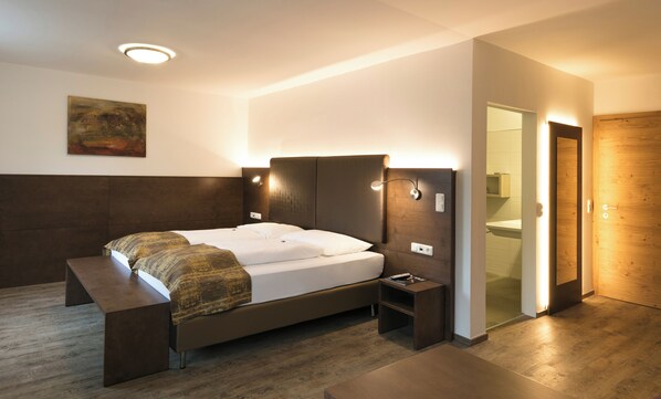 A modern hotel room with a bed, bedside table, bench, and a painting on the wall.