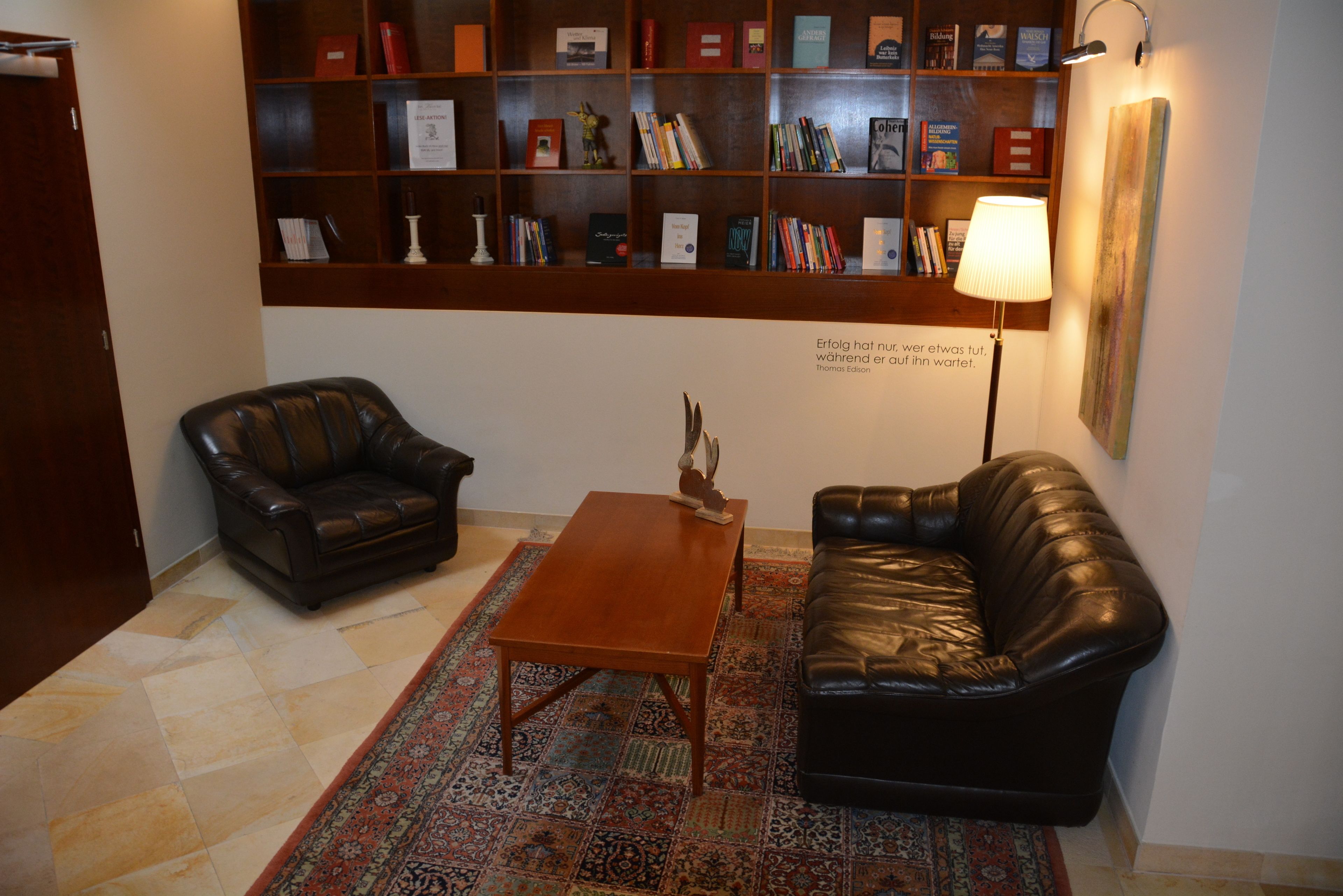 Una habitación con dos sofás de cuero, una mesa de centro de madera, un tapete estampado y una estantería llena de libros.