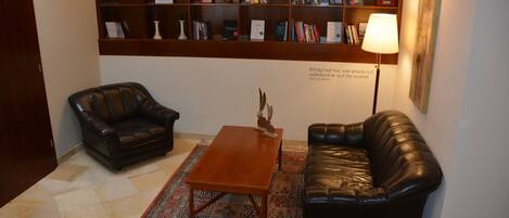 Una habitación con dos sofás de cuero, una mesa de centro de madera, un tapete estampado y una estantería llena de libros.