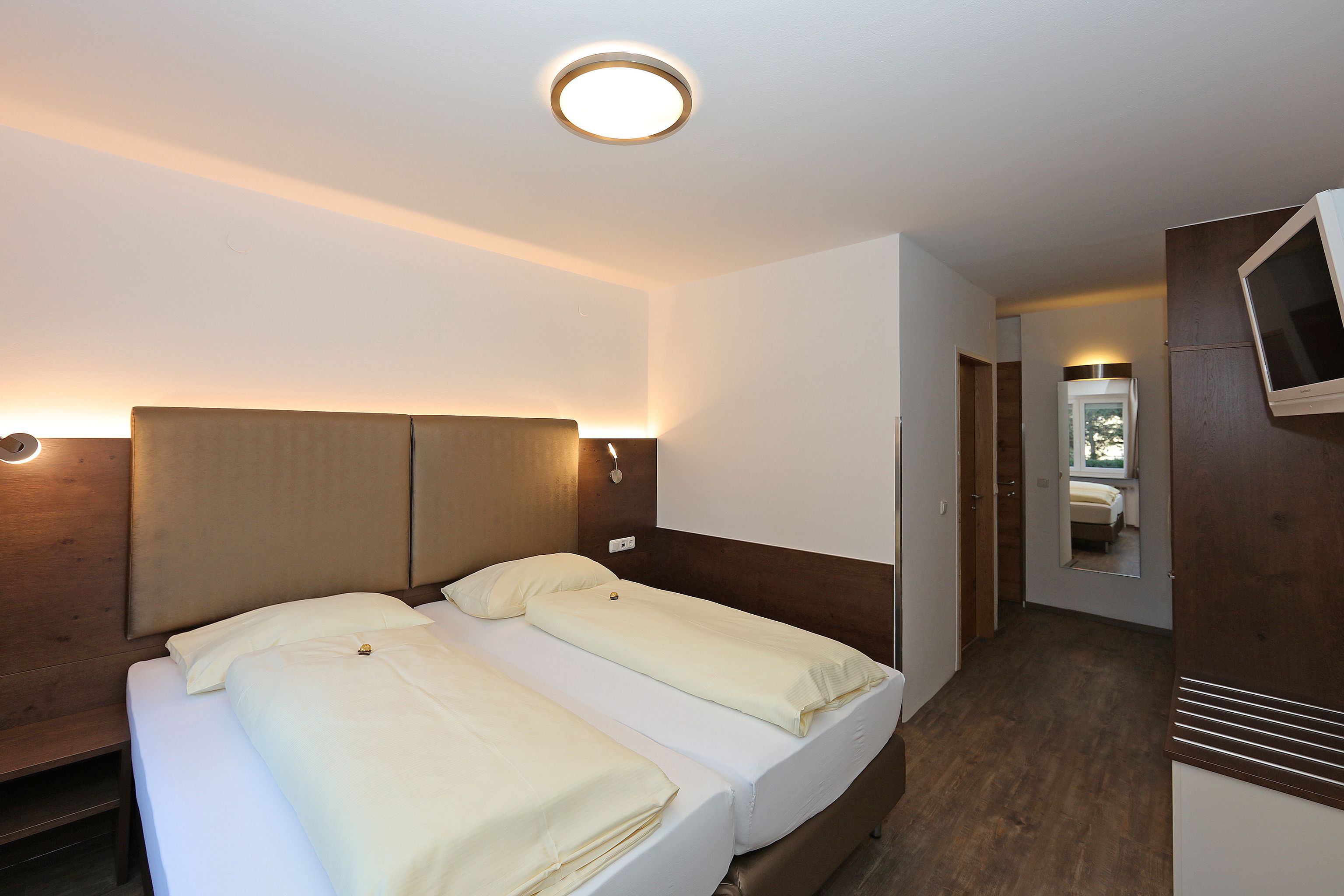 A hotel room with two beds, a TV, and a mirror.