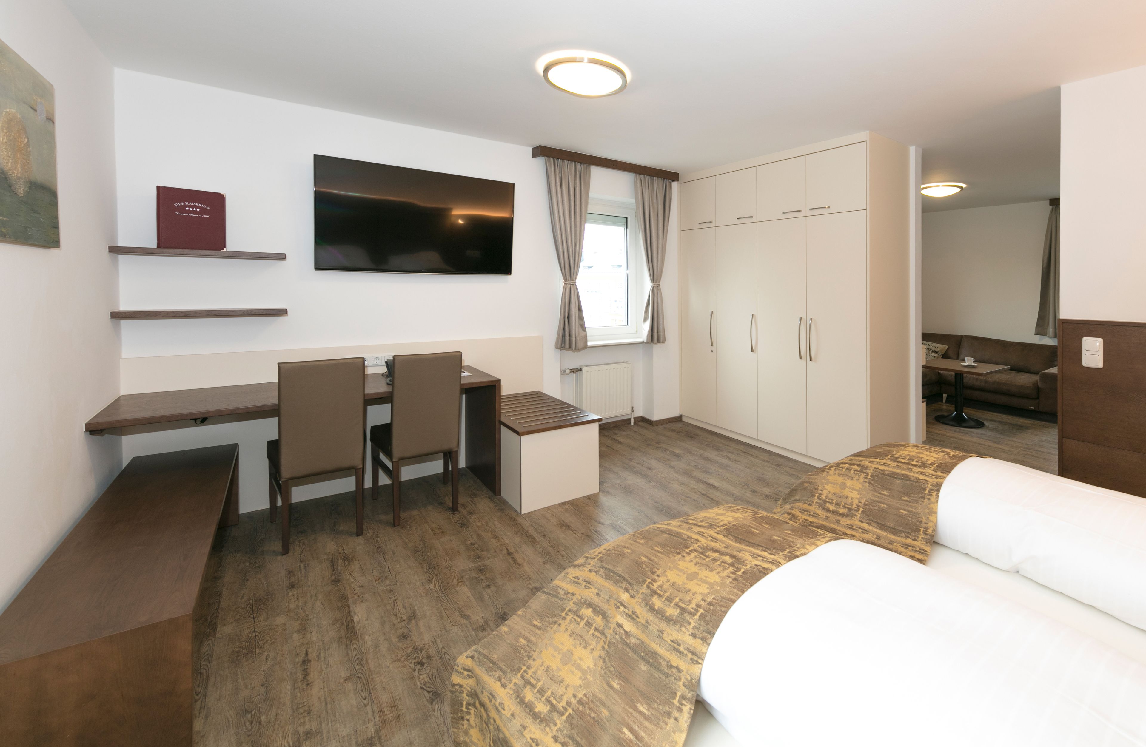 A modern hotel room with a bed, a desk, a chair, a TV, and a wardrobe.