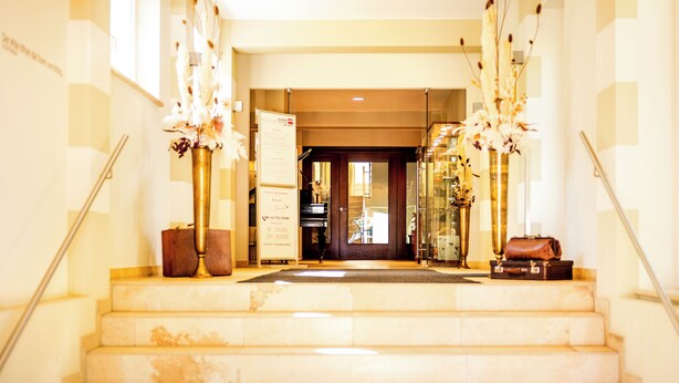 Vestíbulo de hotel con escaleras de mármol, mostrador de recepción y arreglos florales decorativos.