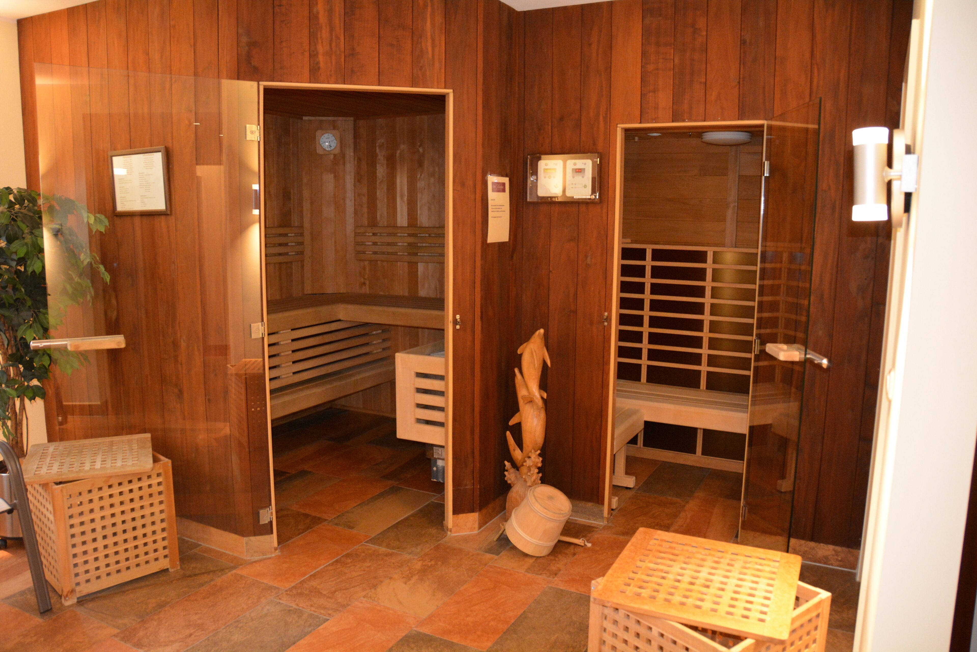 Área de spa com piso de madeira, sauna, mesa de massagem e um pequeno banco de madeira.