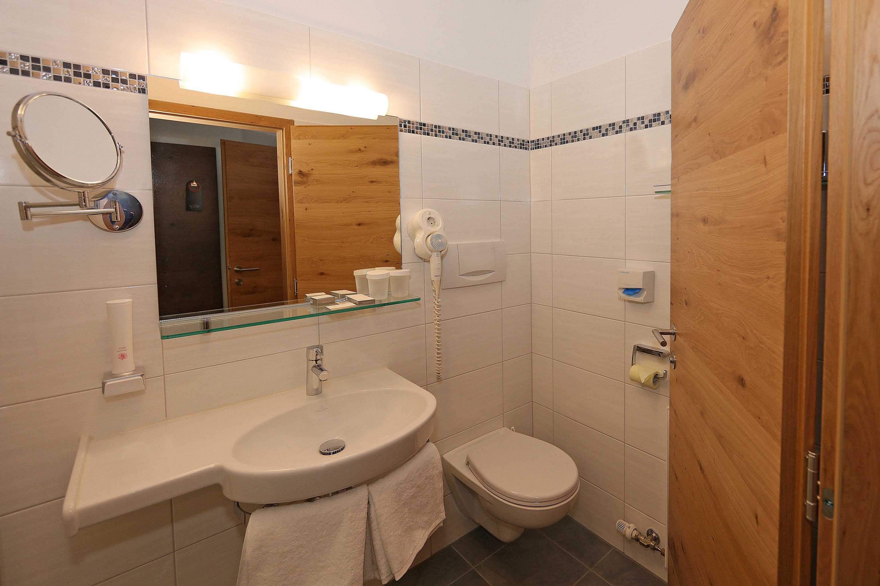 A bathroom with a sink, mirror, toilet, and shower area.