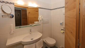 A bathroom with a sink, mirror, toilet, and shower area.