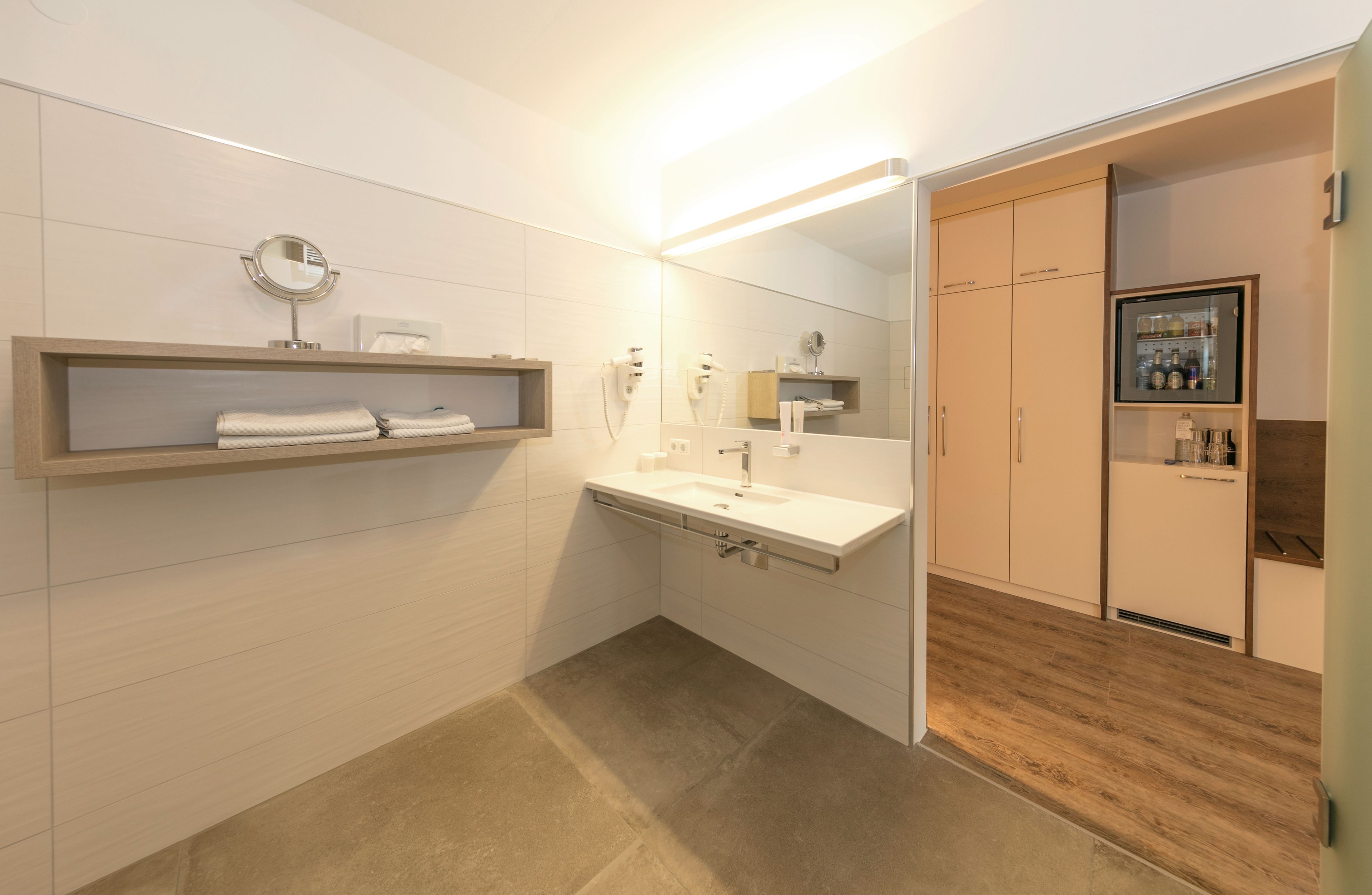 A modern bathroom with a vanity, mirror, towel rack, and a built-in cabinet with toiletries.
