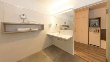 A modern bathroom with a vanity, mirror, towel rack, and a built-in cabinet with toiletries.