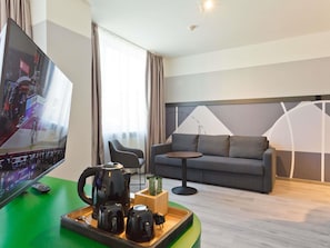 A modern hotel room with a flat-screen TV, a sofa, a small table, and a coffee station.