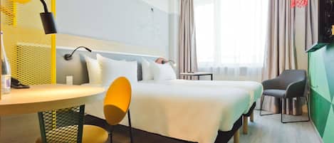 A hotel room with a bed, a desk with a chair, a TV, and a window with curtains.