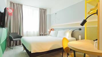 A hotel room with a bed, a desk, a chair, a TV, and a window with curtains.
