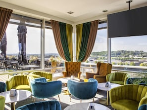 Una habitación de hotel moderna con ventanas amplias, un balcón con mobiliario exterior y vistas a la ciudad.
