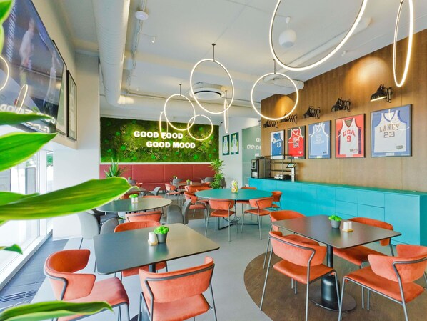 Ein Restaurantinnenraum mit Tischen und Stühlen, einer Wand mit der Aufschrift 'GOOD FOOD GOOD MOOD' und Sporttrikots an der Wand.